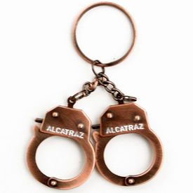 A Bronze color metal handcuff key chain with "Alcatraz" printed on the cuffs.